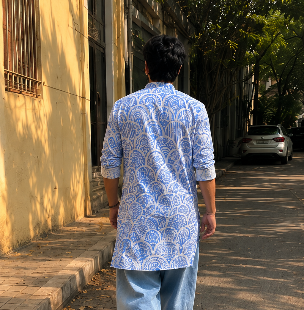 Person wearing a blue patterned shirt and light blue pants walking on a street.