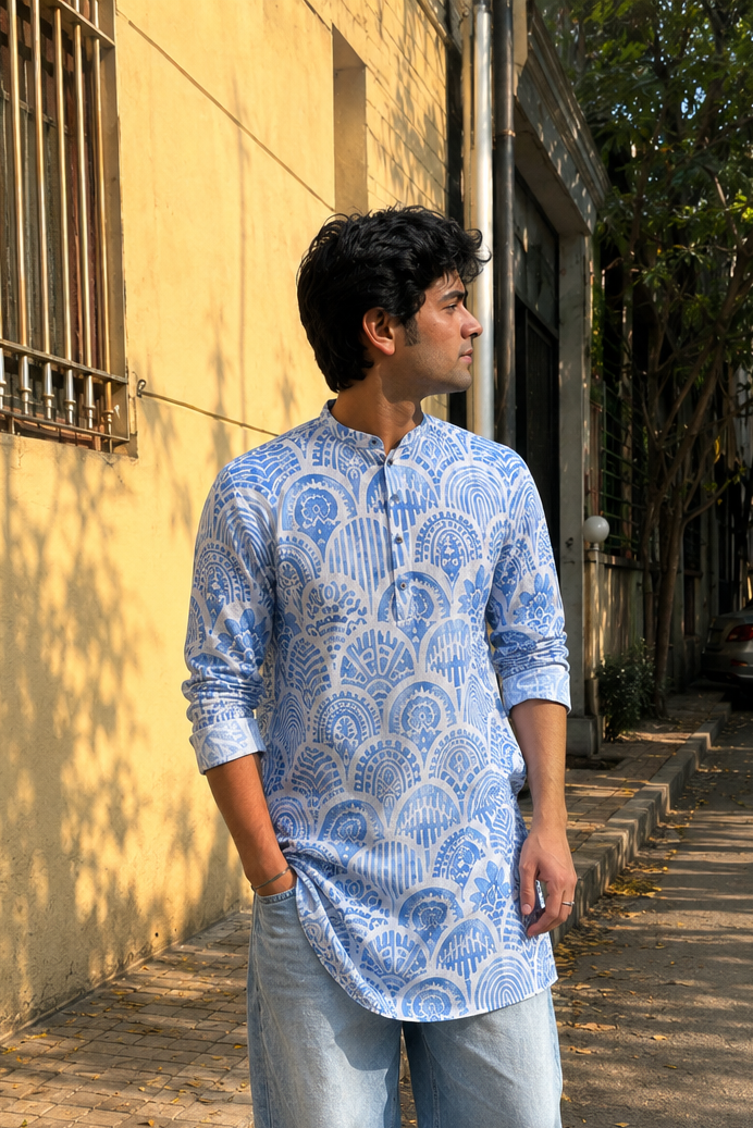 Man wearing a blue patterned kurta with light blue jeans standing on a street.