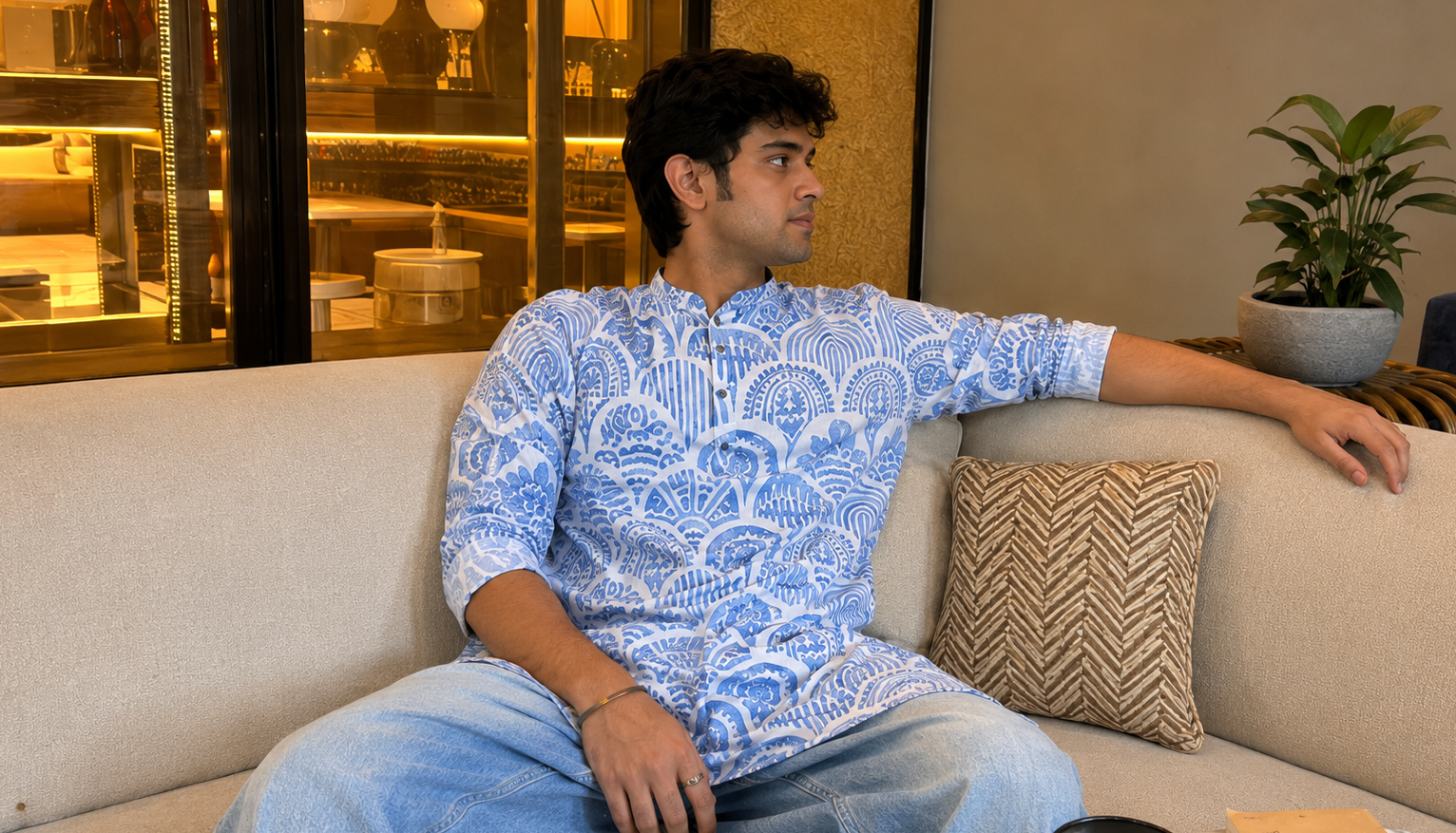Man sitting on a couch wearing a blue patterned shirt in a modern interior setting.
