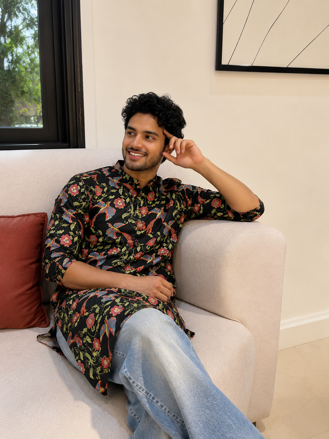 Man sitting on a couch wearing a floral shirt and jeans, smiling.