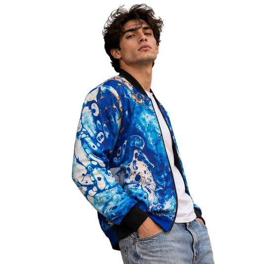 A man wearing a blue and white abstract patterned bomber jacket, a white t-shirt, and light-wash jeans, leaning against a beige stone wall.