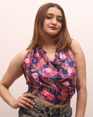 A woman posing in a sleeveless halter crop top with a vibrant pink, purple, and blue flamingo print, paired with high-waisted, faded blue jeans against a plain light background.