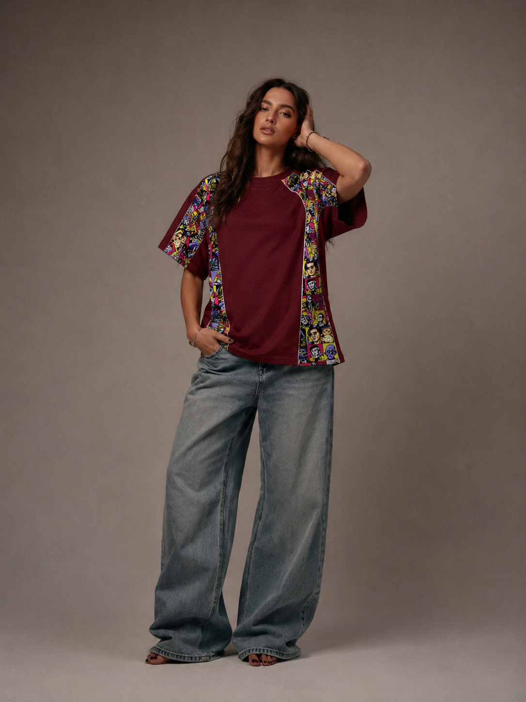 Woman wearing a maroon shirt with a colorful floral kimono-style jacket and blue jeans against a gray background