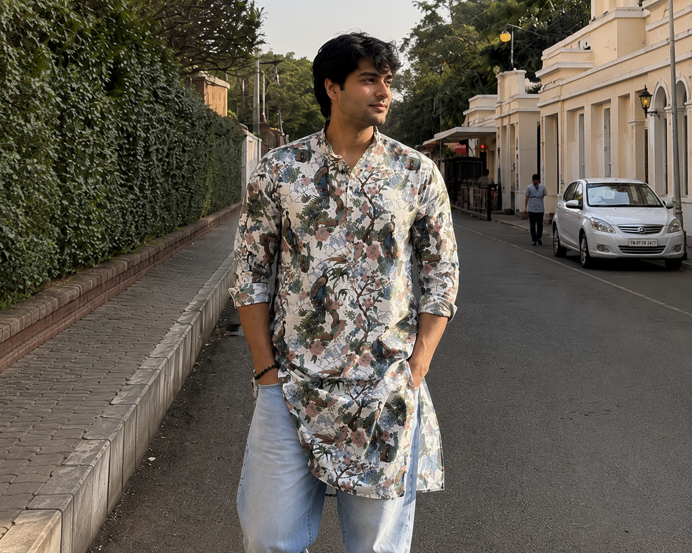 Man in a floral shirt walking on a street with buildings and cars in the background