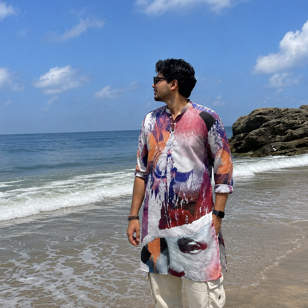 Man standing on a beach wearing a colorful kurta with a blue sky and ocean background