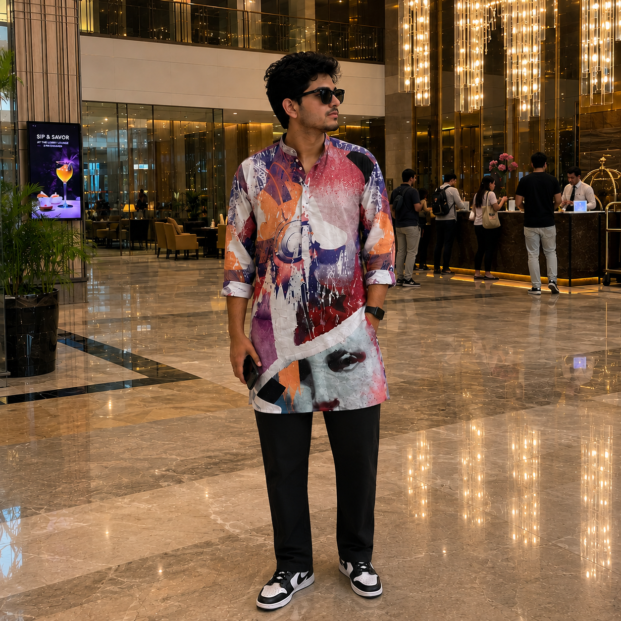 Man in a colorful Kurta standing in a modern indoor setting with people and decor.
