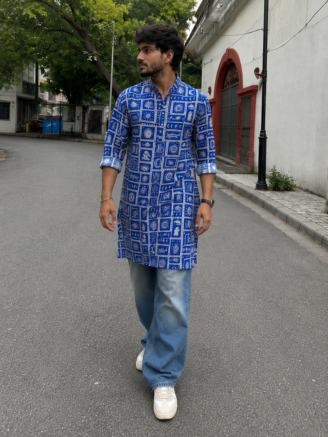 Man wearing a blue patterned kurta with light blue jeans walking on a street.