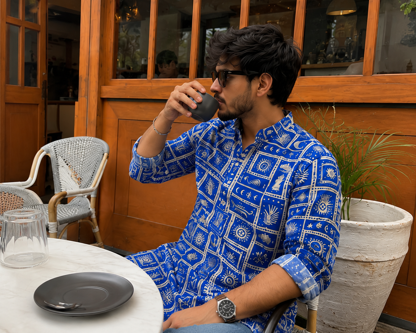 Man in a blue patterned kurta drinking from a cup outdoors.