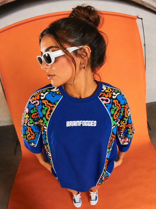 Person wearing a blue sweatshirt with 'BRAINFUGGED' text, colorful sleeves, and white sunglasses on an orange chair.