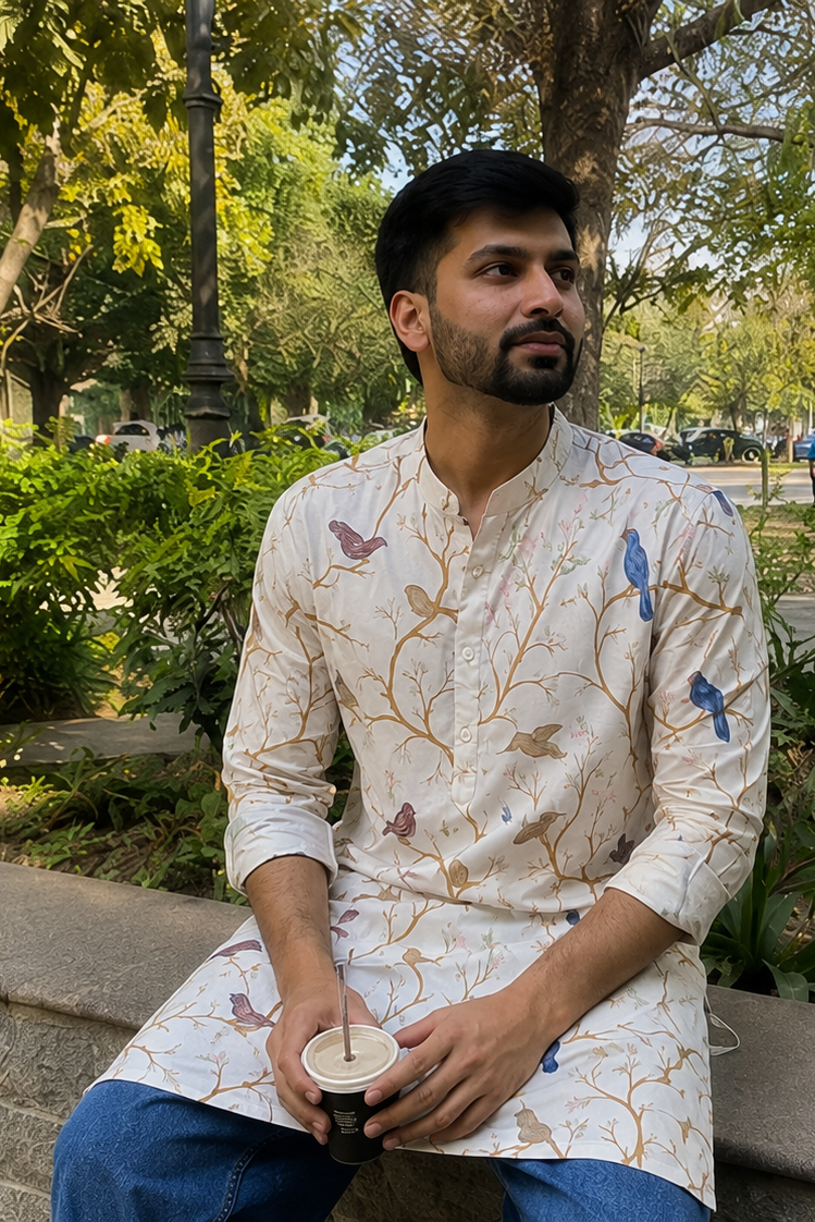 Man sitting outdoors in a park holding a cup, wearing a patterned kurta.