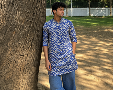 Man wearing a blue patterned kurta standing next to a tree