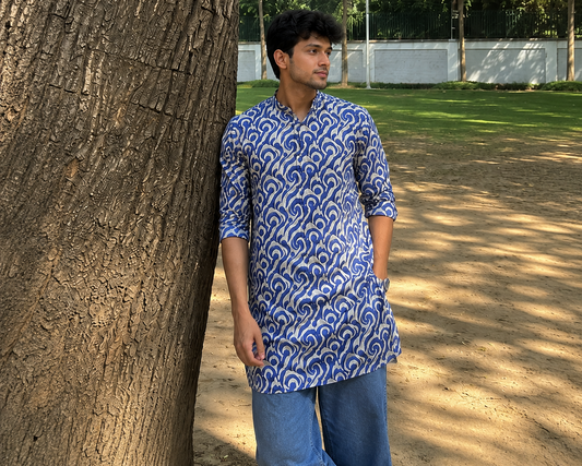 Man wearing a blue patterned kurta standing next to a tree