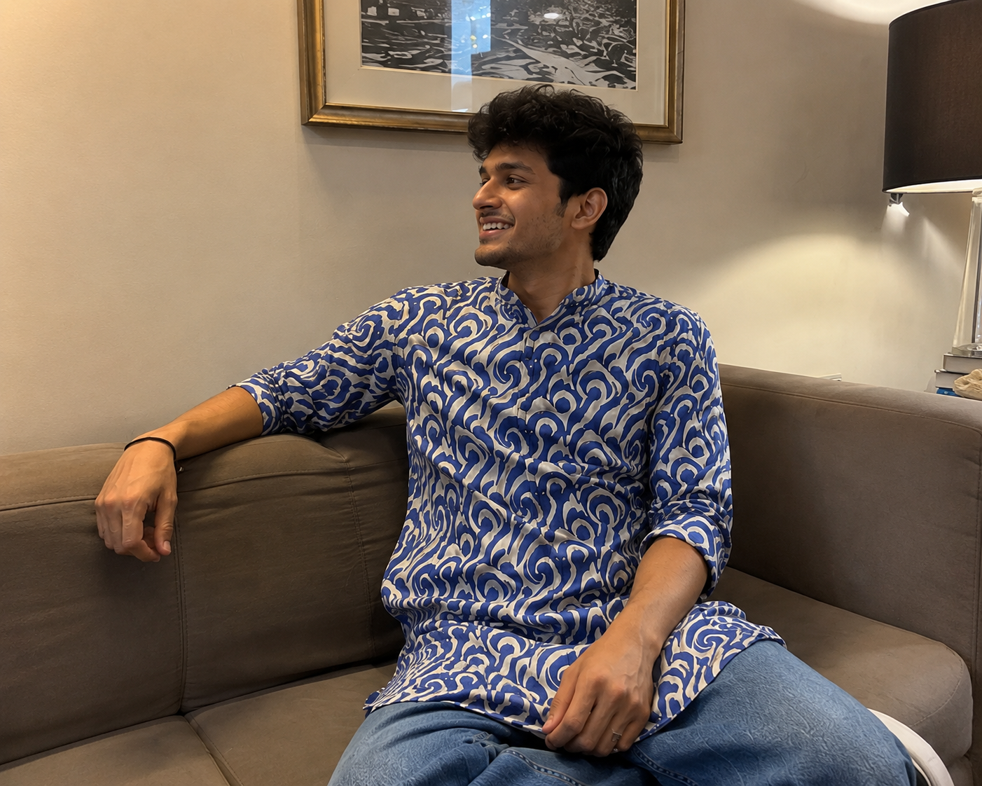 Man sitting on a couch wearing a blue patterned shirt in a living room setting.