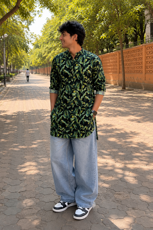 Man wearing a green patterned kurta and blue jeans standing on a tree-lined street.