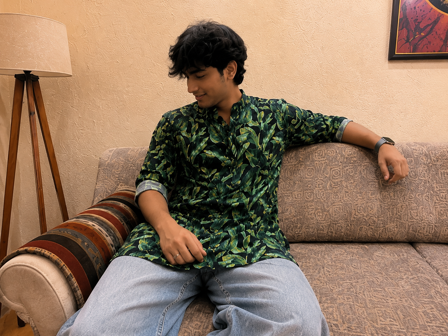 Person wearing a green patterned Kurta sitting on a couch in a living room.