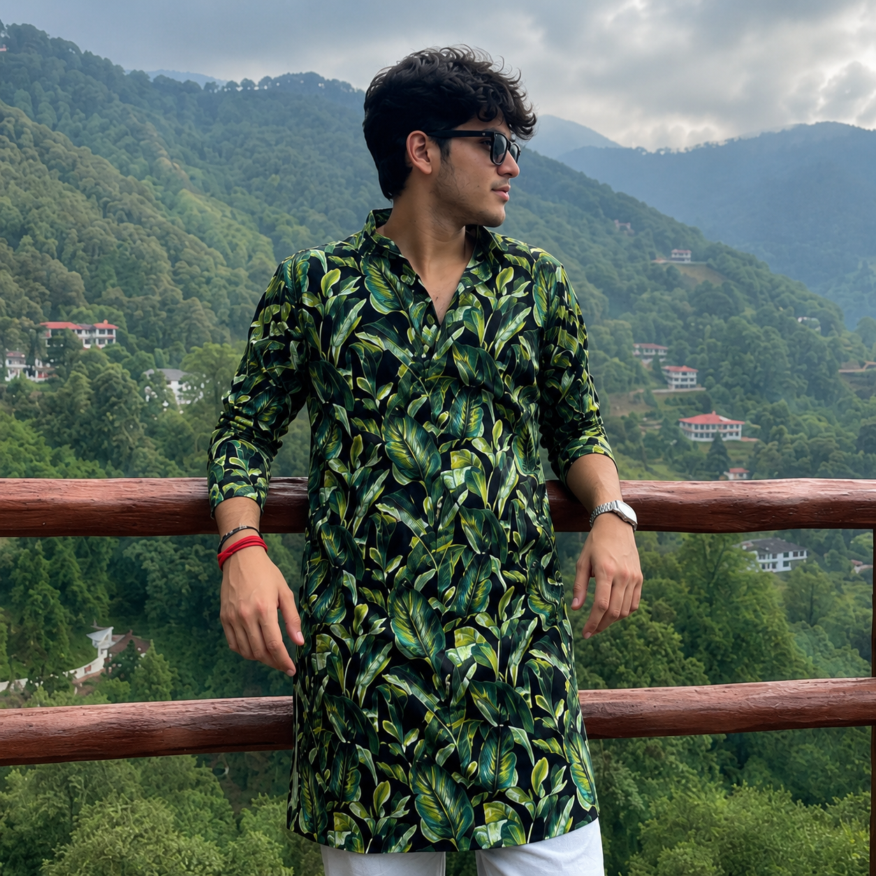 Man wearing a green leaf-patterned kurta standing against a scenic mountain backdrop.