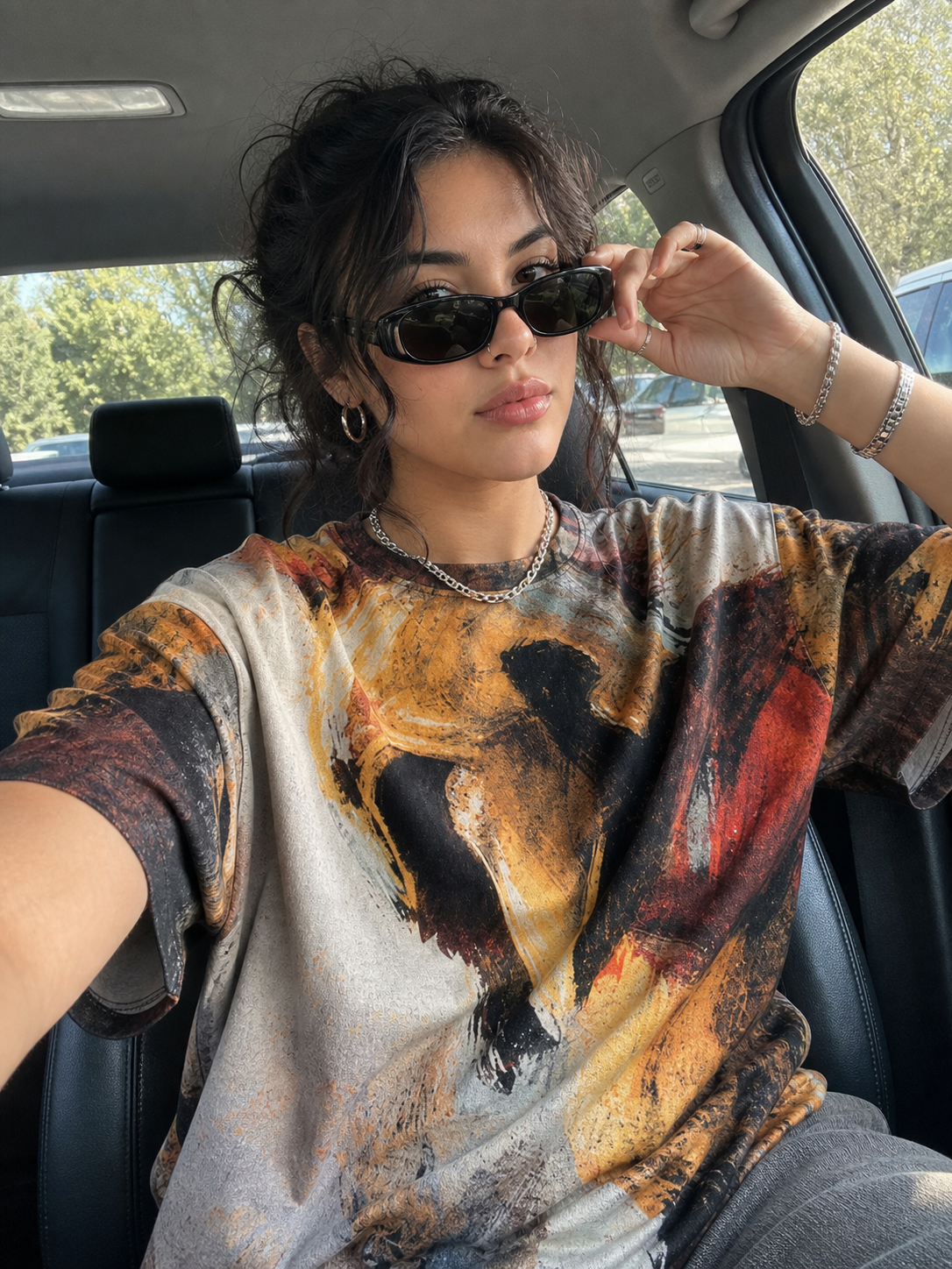 Woman wearing a tie-dye shirt sitting inside a car.