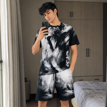 Man taking a mirror selfie wearing a black and white tie-dye outfit in a bedroom.