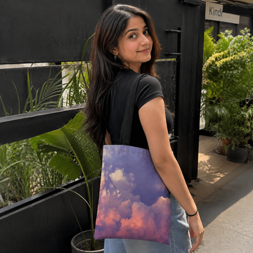 Woman holding a tote bag with a colorful cloud design outdoors.