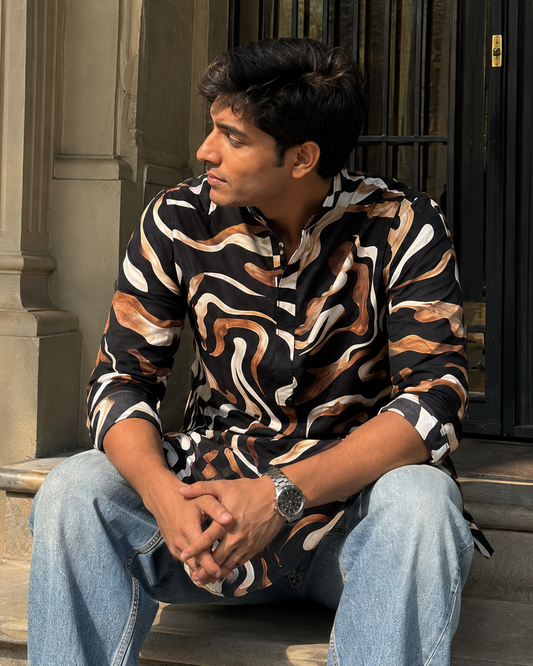 Man sitting on steps wearing a patterned shirt and jeans, with a building in the background.
