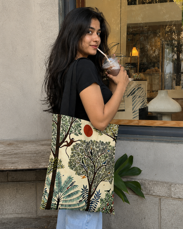 Woman holding a patterned tote bag with a drink, standing outside a building.