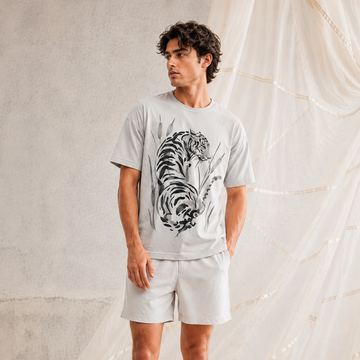 Man wearing a gray t-shirt with a tiger design and light gray shorts against a neutral background.