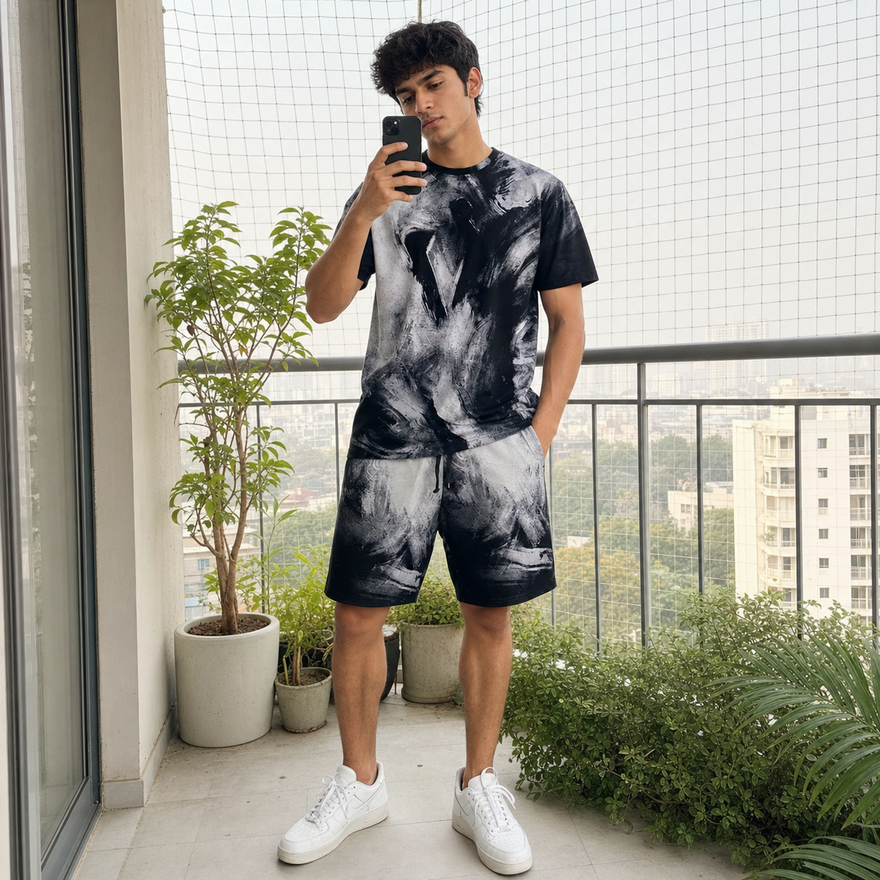 Person taking a mirror selfie on a balcony with plants and a cityscape view.